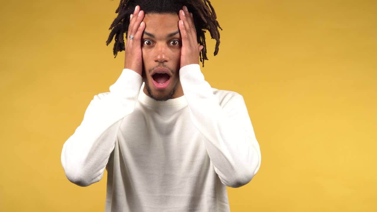 Portrait of young afro american man shocked and confused, yellow background