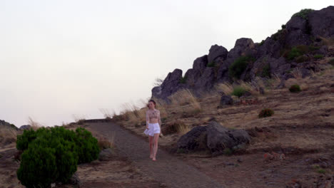 a young blond girl walks alone barefoot along a path on top of the mountain in the fog