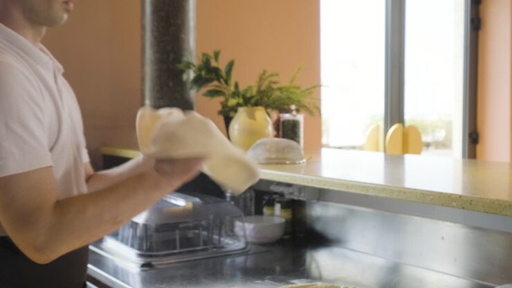 Chef che impasta la pizza su un piano di lavoro e la fa volteggiare in aria in una cucina di ristorante