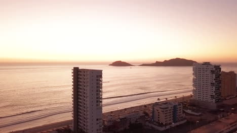 Flying-away-from-beautiful-beach-front-high-rise-buildings-at-sunset