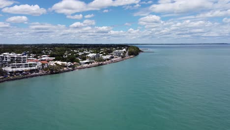 Drone-Ascendiendo-Sobre-El-Océano-Y-Luego-Volando-Hacia-Un-Pueblo-De-Playa