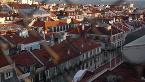 cityscape through fence of lisbon, portugal, with river tejo in background during sunset