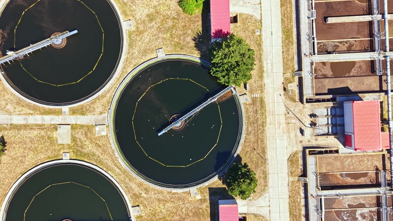 Water treatment plant viewed from above showing circular tanks with water and equipment around them