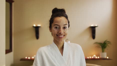 Portrait-of-happy-biracial-woman-in-robe-standing-in-bathroom-and-looking-at-camera