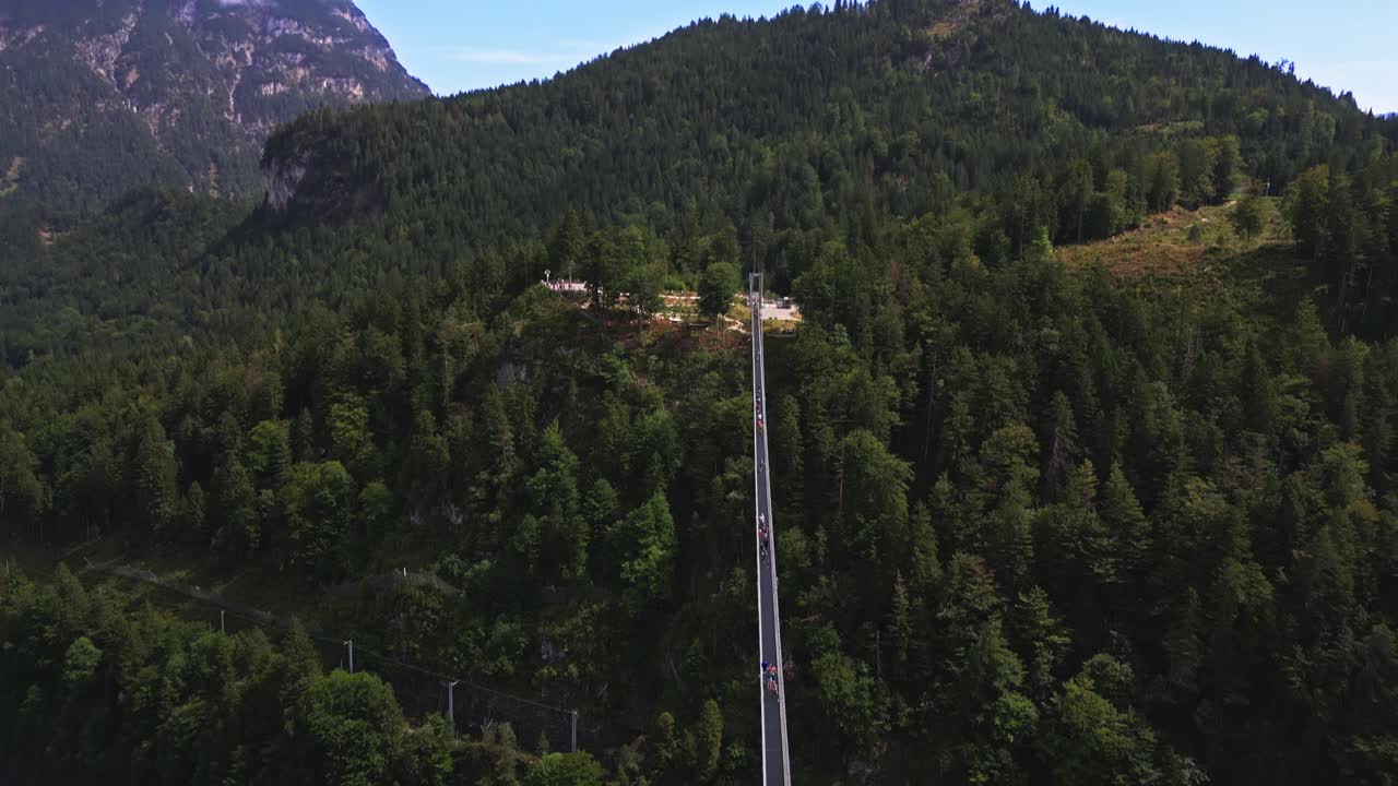 Panoramic aerial view of the world's longest pedestrian suspension bridge leading to Ehrenberg Castle in Austria, over a busy road, surrounded by a forest of trees
