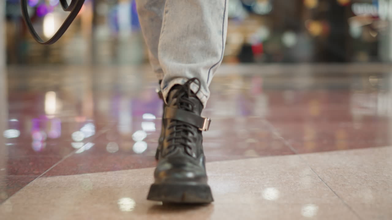 close up leg view of graceful woman in chunky black boots stepping forward on glossy tiled mall floor under bright overhead lights capturing elegant motion and modern style atmosphere