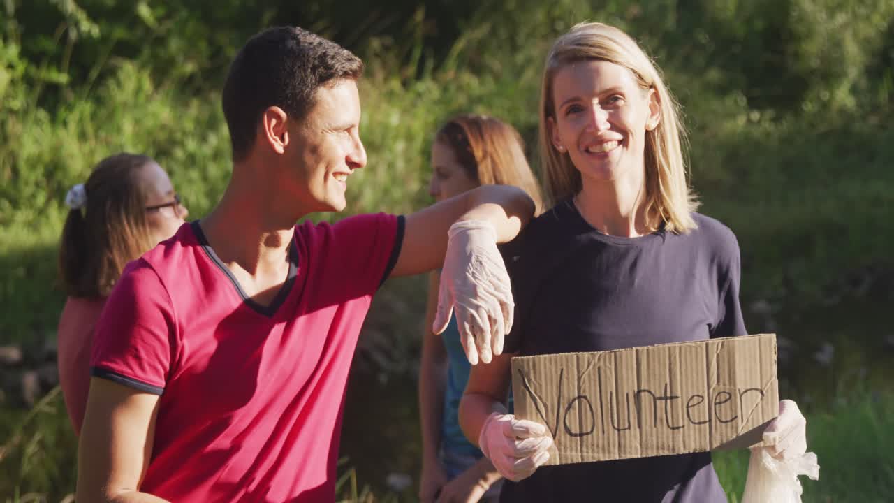 adulto medio sonriendo y mirando a la cámara con una mujer sosteniendo un cartel de voluntario durante el día de limpieza del río