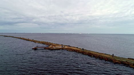 Aerial-drone-forward-moving-shot-over-a-rocky-road-extending-into-the-sea-on-a-cloudy-day