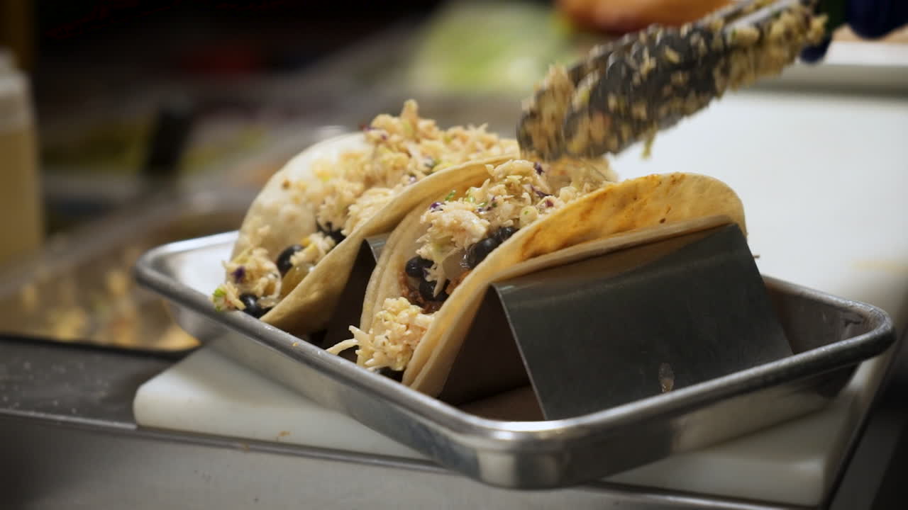 el chef encabeza los tacos de frijoles negros de pescado con ensalada de repollo, cocina los tacos en el puesto de tacos con ensalada de col, cámara lenta de cerca 4k
