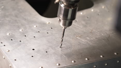 close up of drill bit penetrating aluminum sheet, creating precise holes in a metalwork production process