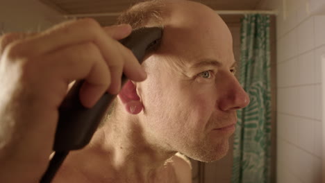 wide shot, a man in a bathroom starts shaving his head