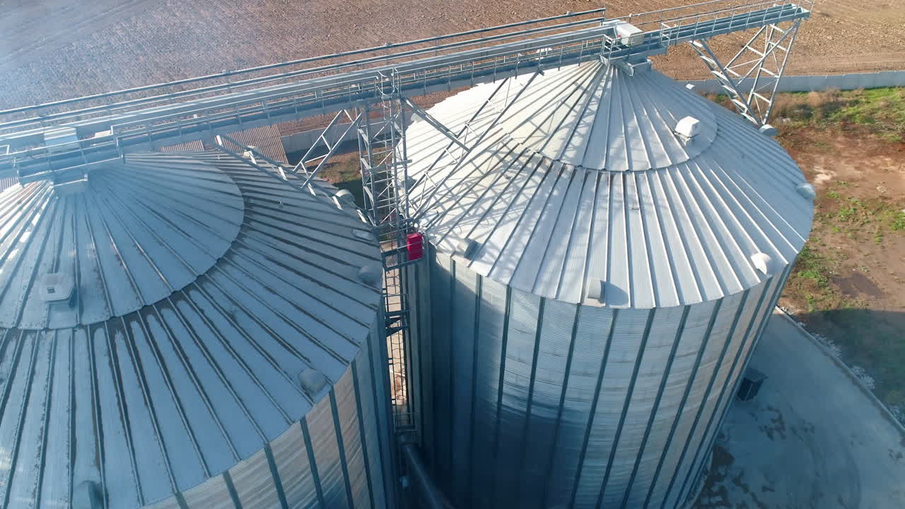 Metal silos on field. Large containers for storing and processing grains. Silver grain elevators in farmland. Aerial view.