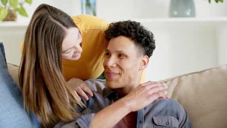 retrato de una feliz pareja diversa sentada en el sofá y abrazándose en casa, en cámara lenta