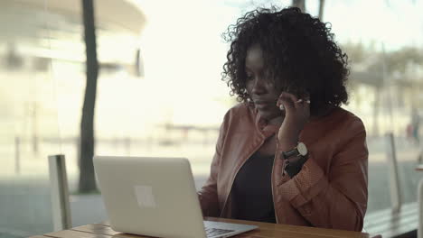 Young-woman-talking-by-cell-phone-and-using-laptop-in-cafe