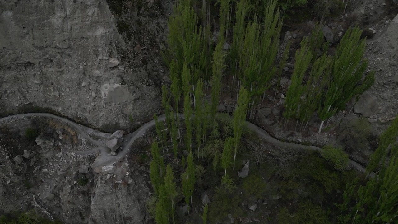 aerial top down drone zoom of rocky riverbed and steep shrub-covered slopes of Karimabad Glacier Valley.