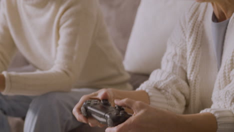 two happy senior women playing video game sitting on sofa