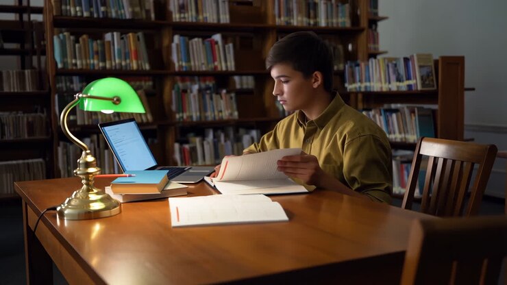 Studerende, der studerer på et bibliotek med bærbar computer og bøger