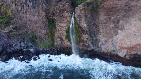 Waterfall-Flowing-into-Ocean-on-Sea-Cliff-on-Madeira-Island,-Portugal---Aerial