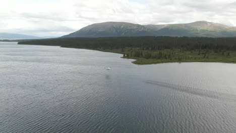 aerial footage of a float plane taking off from a remote lake with mountains and forest in the background