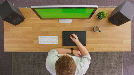 overhead view of male graphic designer or retoucher working at computer with green screen in office