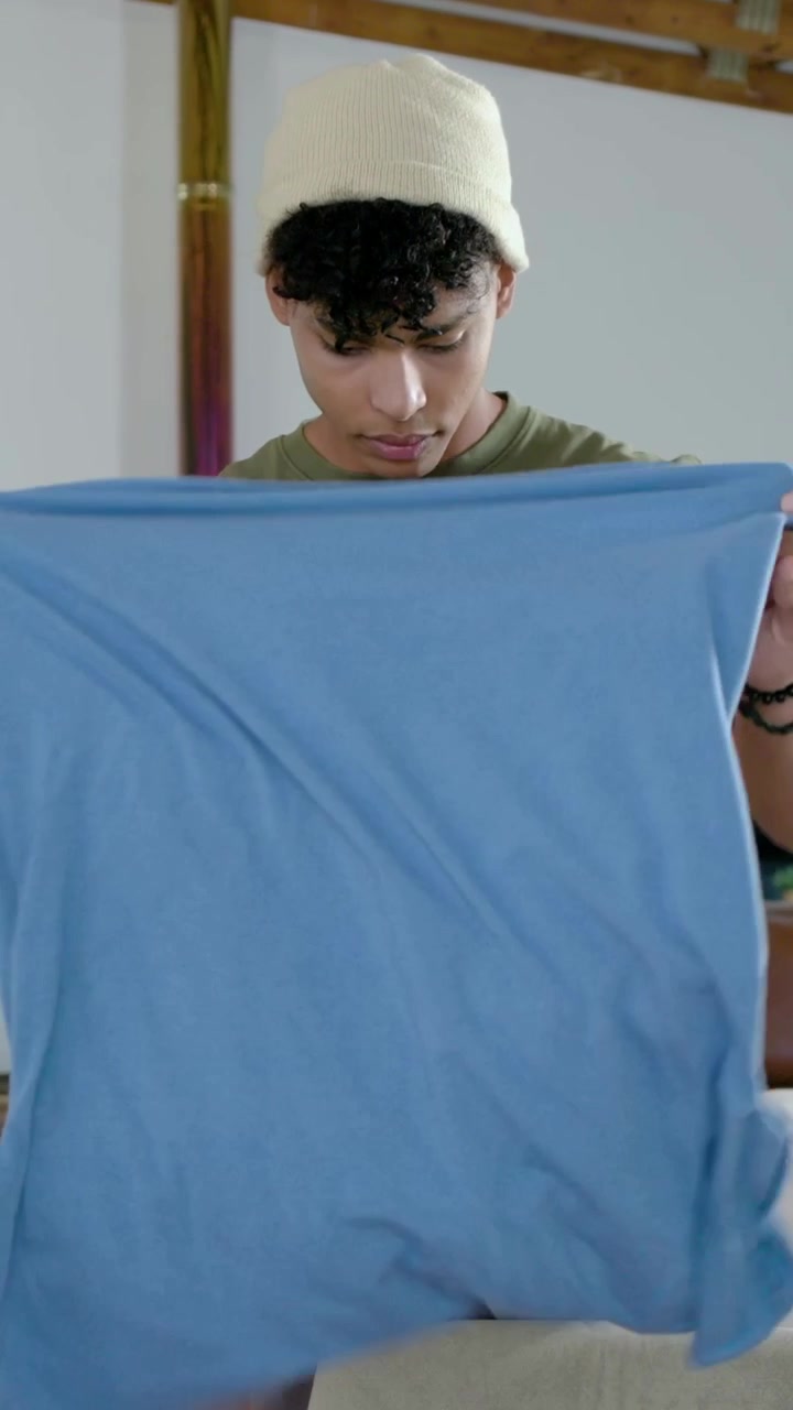 Vertical video: Reaching man in olive tee taking shirts from basket at home, folding neat stack