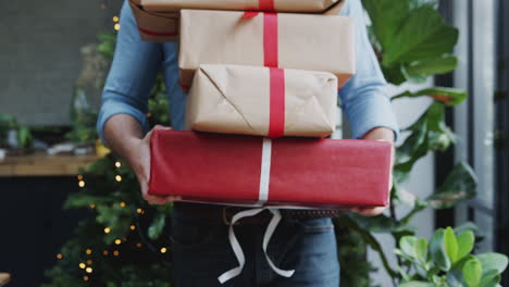 close up of man carrying pile of christmas presents walking towards camera