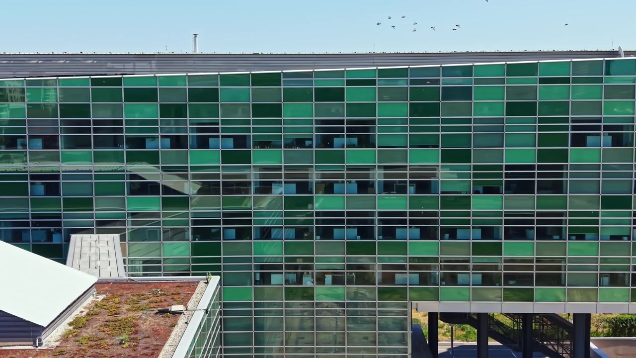 Edifício moderno com vidro verde a céu aberto sob luz solar intensa com árvores ao fundo