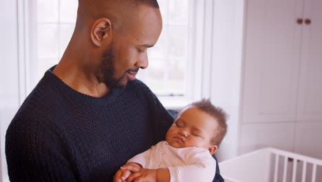 new father cuddling sleeping baby girl in nursery at home