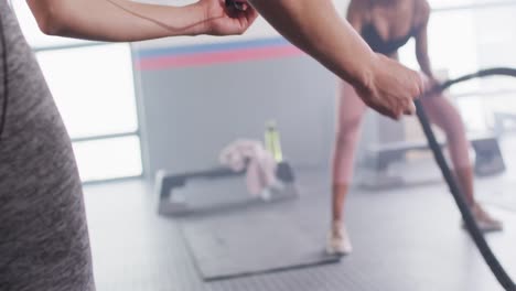 Video-De-Una-Entrenadora-Femenina-Diversa-Con-Cronómetro-Y-Una-Mujer-Luchando-Contra-Cuerdas-Haciendo-Ejercicio-En-Un-Gimnasio