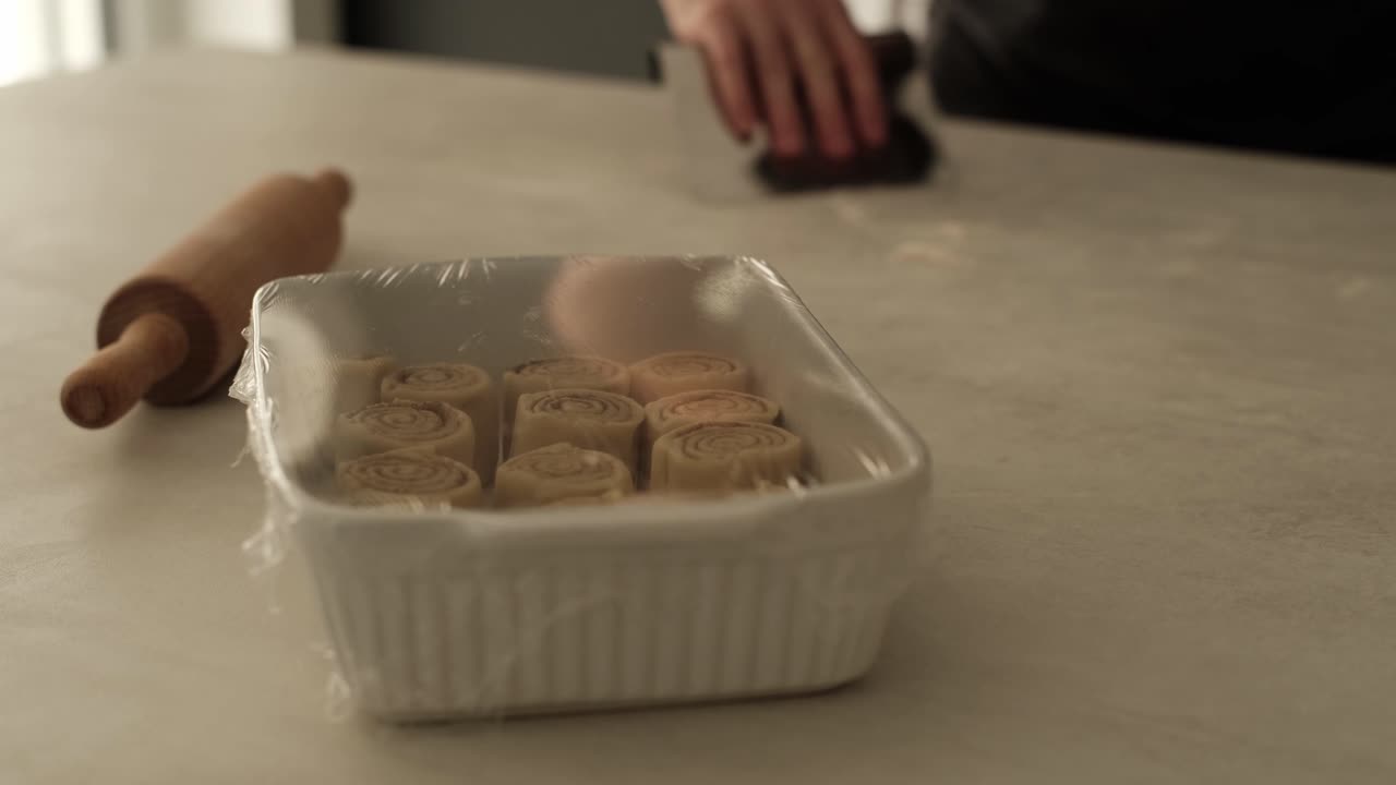 Rising cinnamon buns with a white male cleaning up his workspace after cooking in the background