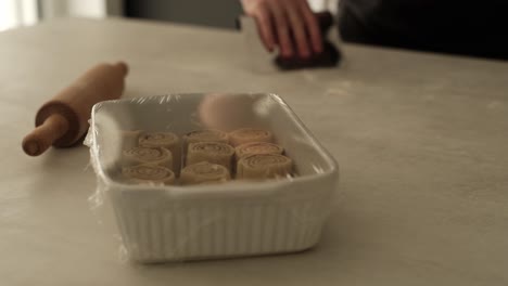 Bollos-De-Canela-En-Aumento-Con-Un-Hombre-Blanco-Limpiando-Su-Espacio-De-Trabajo-Después-De-Cocinar-En-El-Fondo