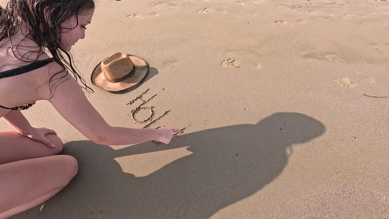 On a warm, sunny day at the beach, a young girl kneels in the sand, delicately reaching for a small creature as she enjoys the simplicity of nature