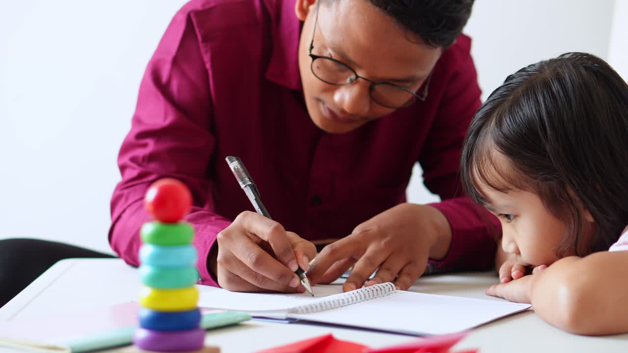 Tålmodig asiatisk veileder forklarer grammatikk til en fokusert liten jente under privatundervisning.