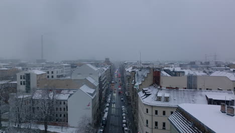 Forwards-fly-above-winter-city.-Snowing-in-urban-neighbourhood.-Street-lined-by-multistorey-apartment-houses.-Berlin,-Germany