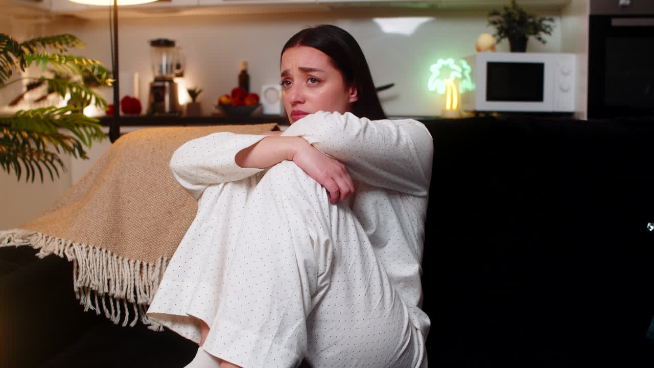 Young woman sits hugging knees sadness bad news stress depression upset sigh looks down at evening