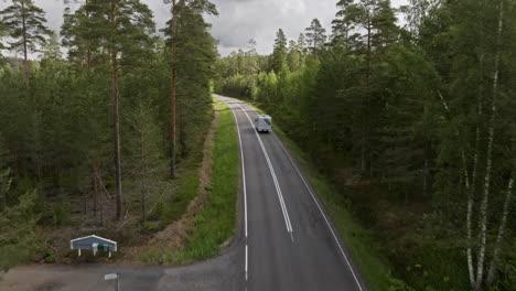 aerial view following a camper van driving on a forest road in finland, sunny day