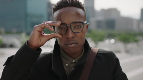 close up portrait of young trendy african american man student puts on glasses looking at camera smiling confident in urban city background