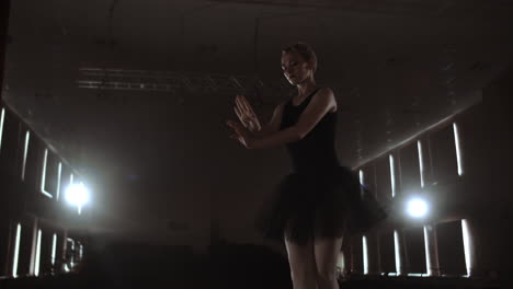 graciosa mujer bailarina en un vestido oscuro en un escenario oscuro del teatro en el humo realiza movimientos de baile en cámara lenta.