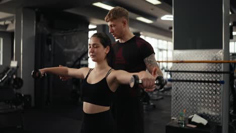 woman lifting weights with personal trainer at gym