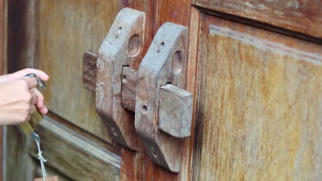 hands unlocking a padlock on a wooden door