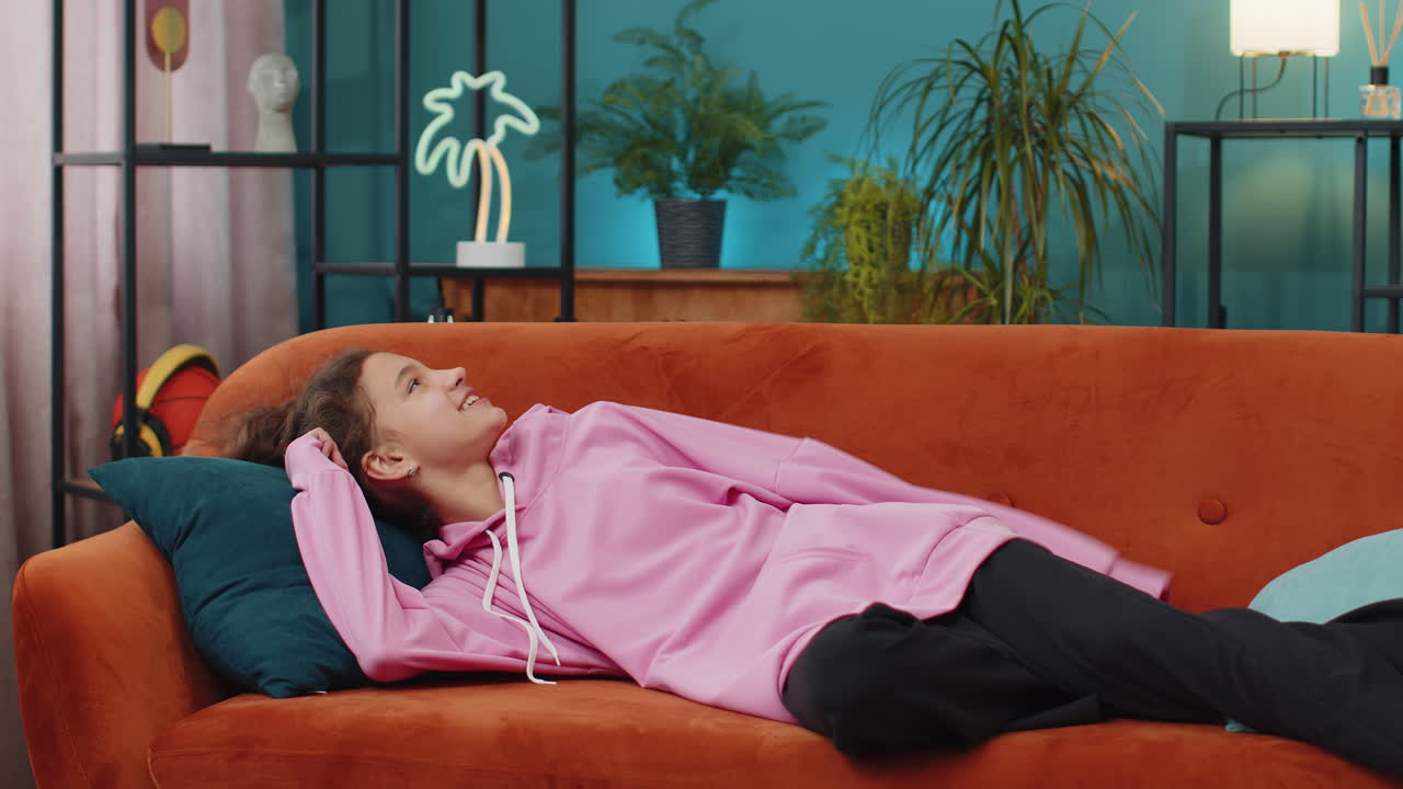 Tired caucasian preteen school girl enters room lying down on couch taking a rest falling asleep