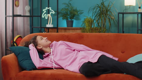 tired caucasian preteen school girl enters room lying down on couch taking a rest falling asleep