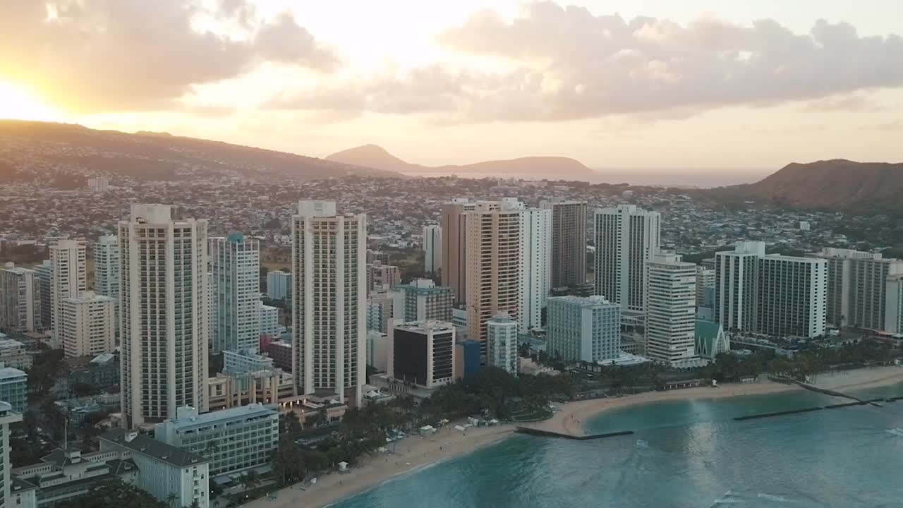 Drone aereo in lenta panoramica che sorvola lo skyline colorato di Honolulu al tramonto a Oahu, Hawaii, con la spiaggia di Waikiki come punto di interesse speciale