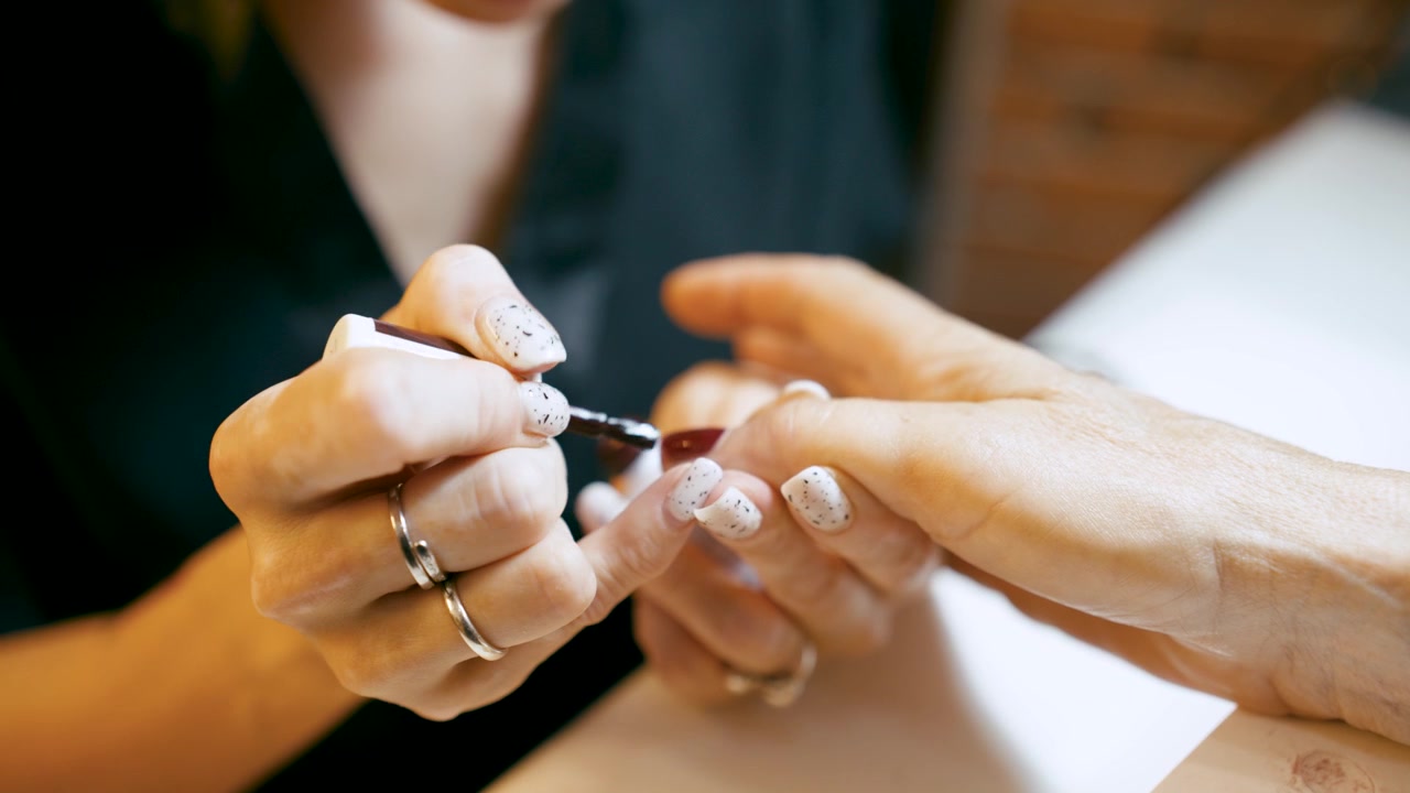 Manicure aplicando esmalte vermelho escuro nas unhas de cliente