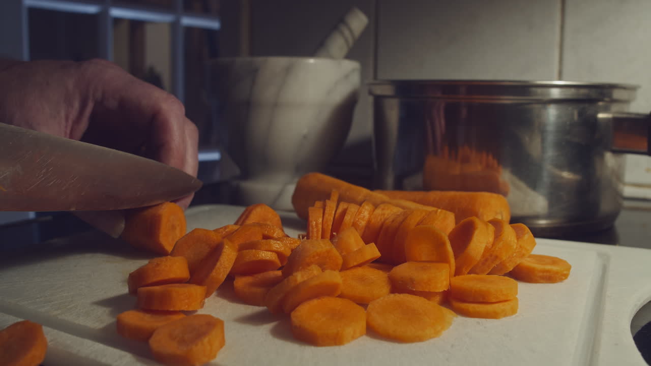 Chopping pile of carrots in kitchen on cutting board