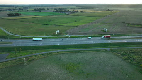 aerial view of a highway with moving vehicles, surrounded by green fields and sparse vegetation, captured during the daytime