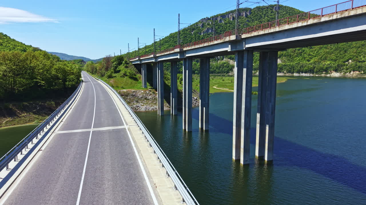 晴天時，在丘陵地區，一條沿河道路的景色，上方有一座橋樑。