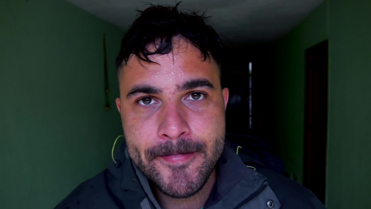 The man approaches the camera with serious look in his eyes, looking like he is tired from working in his heavy duty work