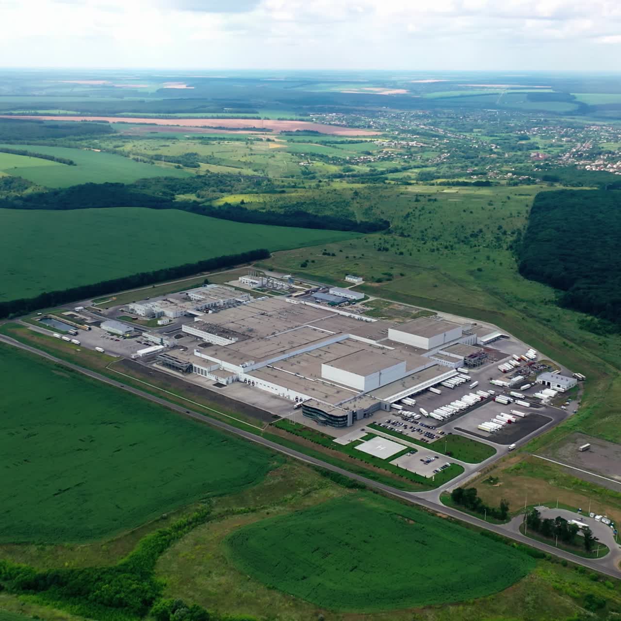 Factory on green landscape. Large industrial territory surrounded by green fields and forests. Manufacturing among nature. Aerial view