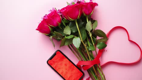 pink roses bouquet with hart shaped bow and mobile phone with copy space screen